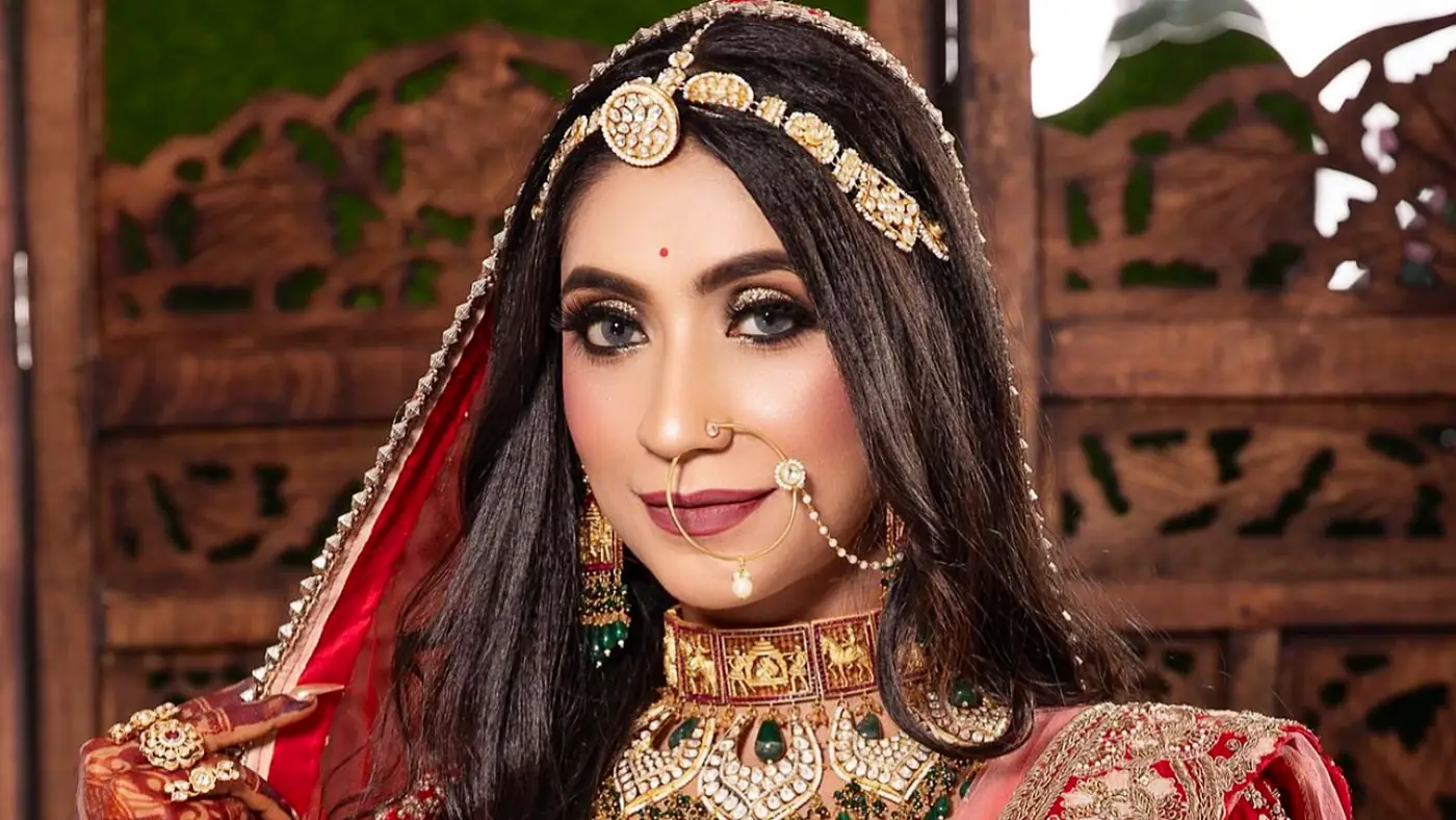 Bride in a red and gold bridal set, make-up by Creative Makeovers, against the studio's carved wood backdrop